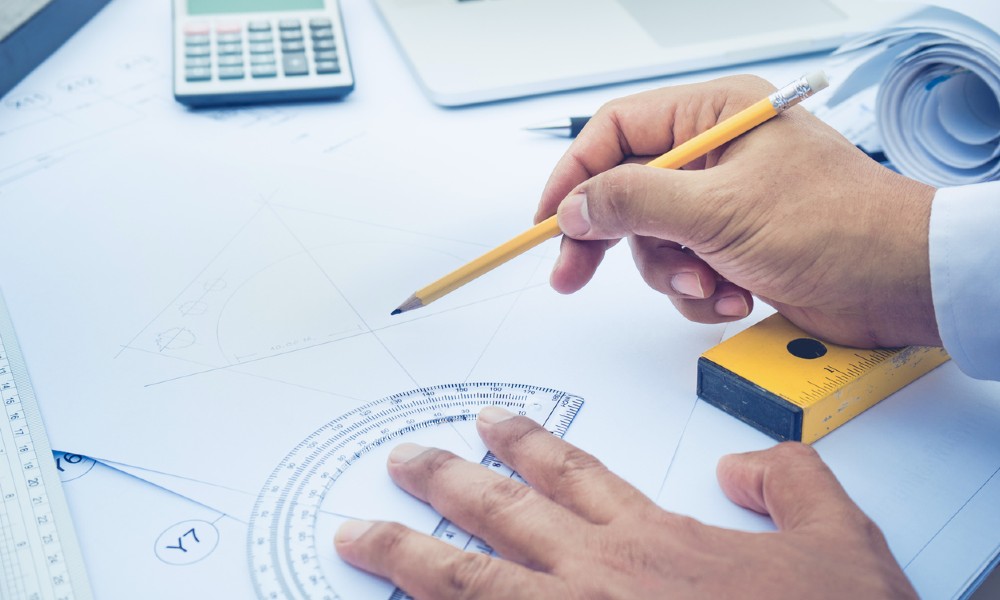 A designer uses drafting tools to draw up a CRE office design that fits the project budget.