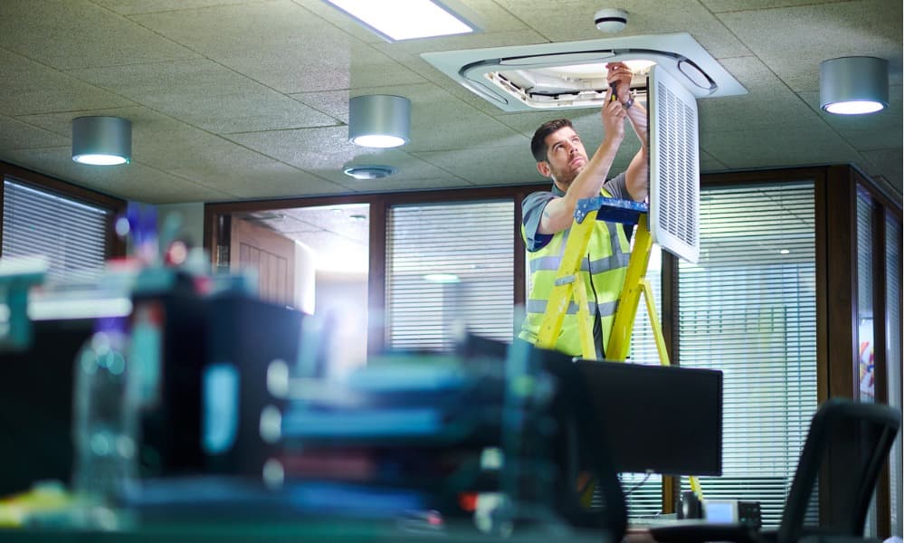 commercial property maintenance personnel working on the HVAC system in an office setting